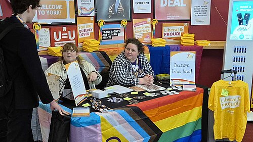 A conference stall with Progress flag and LGBT+ Lib Dem resources